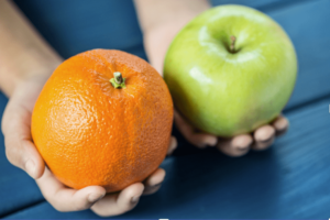 Two hands holding an orange and a green apple.
