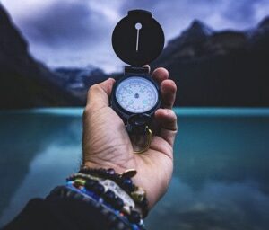 A person holding a compass in front of a body of water.